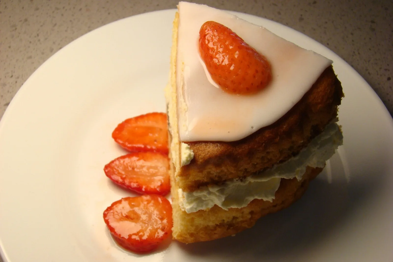 A slice of layered cake topped with a strawberry, more strawberries beside it on a white plate.